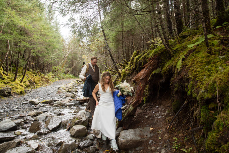 Bride walks in front of groom along a wet rocky trail in Seward Alaska on their hiking elopement day.
