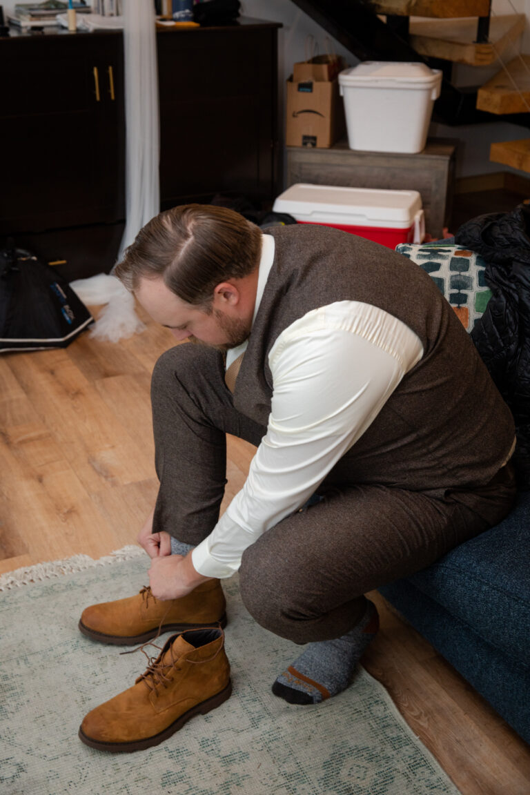 Groom ties his shoes as he gets dressed before his helicopter elopement.