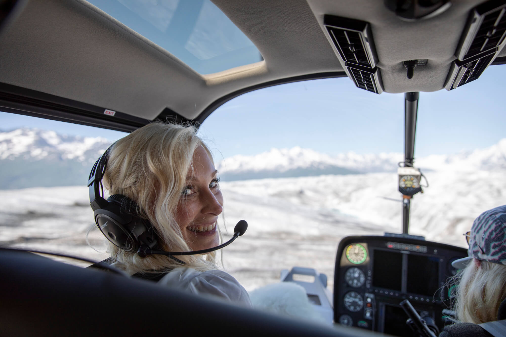 Bride smiling inside a helicopter flying over snowy mountains near Hatcher Pass, Alaska during an elopement experience.