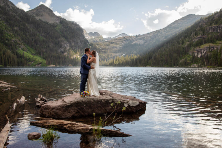 A bride and groom kiss while standing on a rock in the middle of lake in Montana.