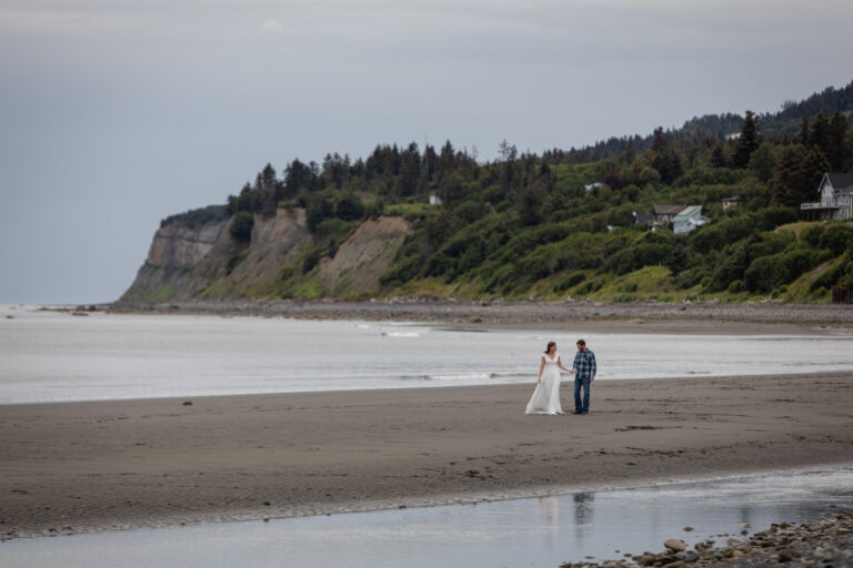 A bride and groom walk along a sandy peninsula in Alaska after their photographers helped them learn how to elope.