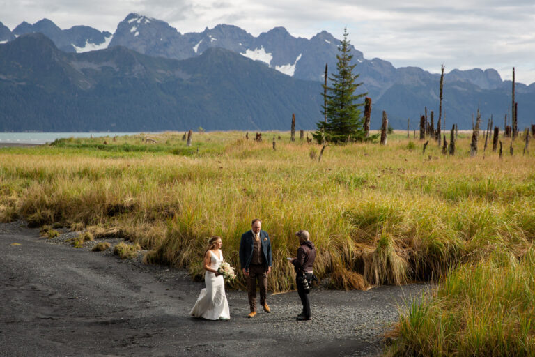 A bride and groom stand on a black sand beach in Alaska talking to their elopement photographer who helped them figure out how to elope.