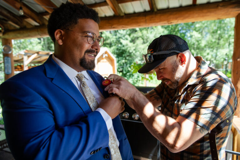 A photographer helps a groom pin his boutonnière to his suit jacket on his elopement day.