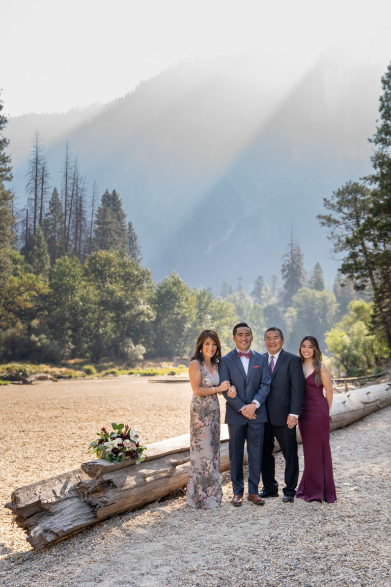 A groom stands with his family in front of a downed tree on a beach in Yosemite