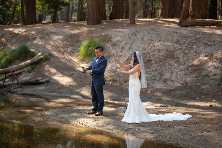 A bride and groom hold fishing poles while standing on a sandy beach in Yosemite.