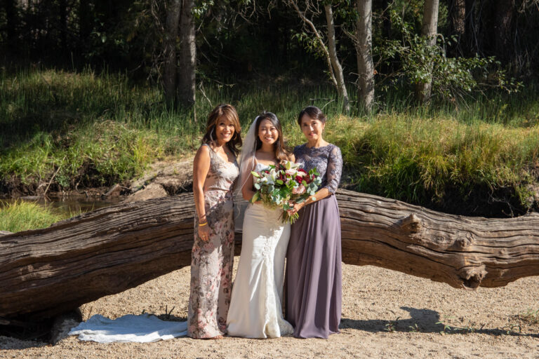 A bride stands between her mom and mother in law on a beach in Yosemite