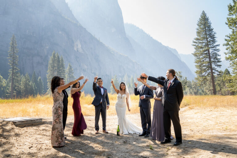 A group of people all raise champagne glasses in the air on a wedding day in Yosemite.