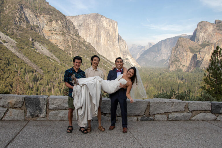 A group of men hold a bride in their arms in front of a stone wall in Yosemite.