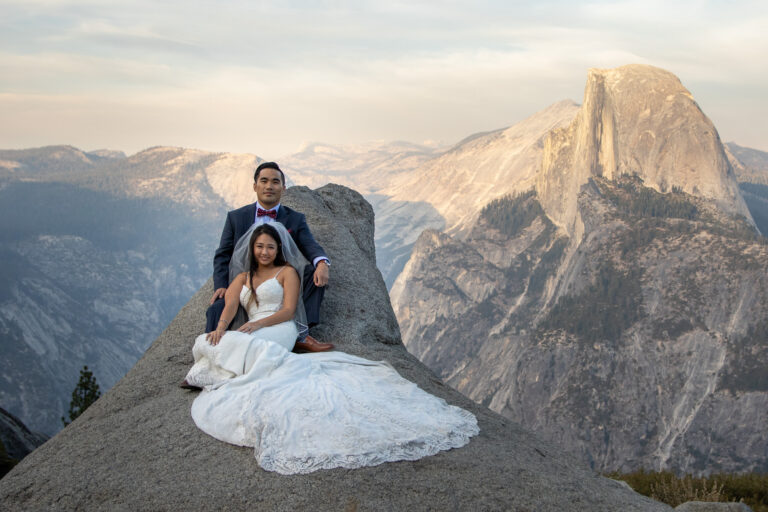 A bride and groom sit on a granite rock in front of Half Dome on their intimate wedding day.