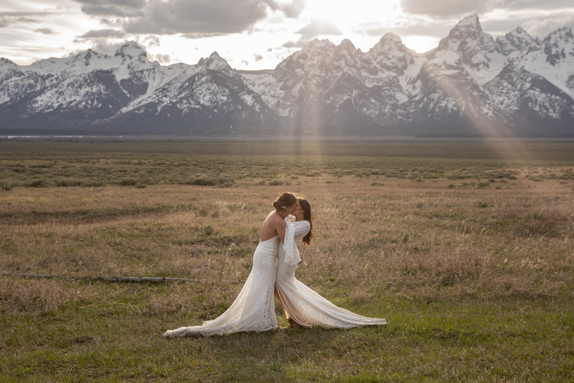Brides share a passionate kiss on their Jackson Hole elopement day, as the sunsets behind them and the Grand Teton mountains glow.