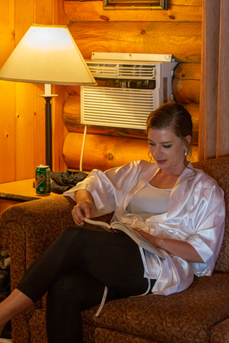 Bride sits in her cabin in Jackson Hole, casually reading a book while waiting for her wife to finish getting ready for their elopement.