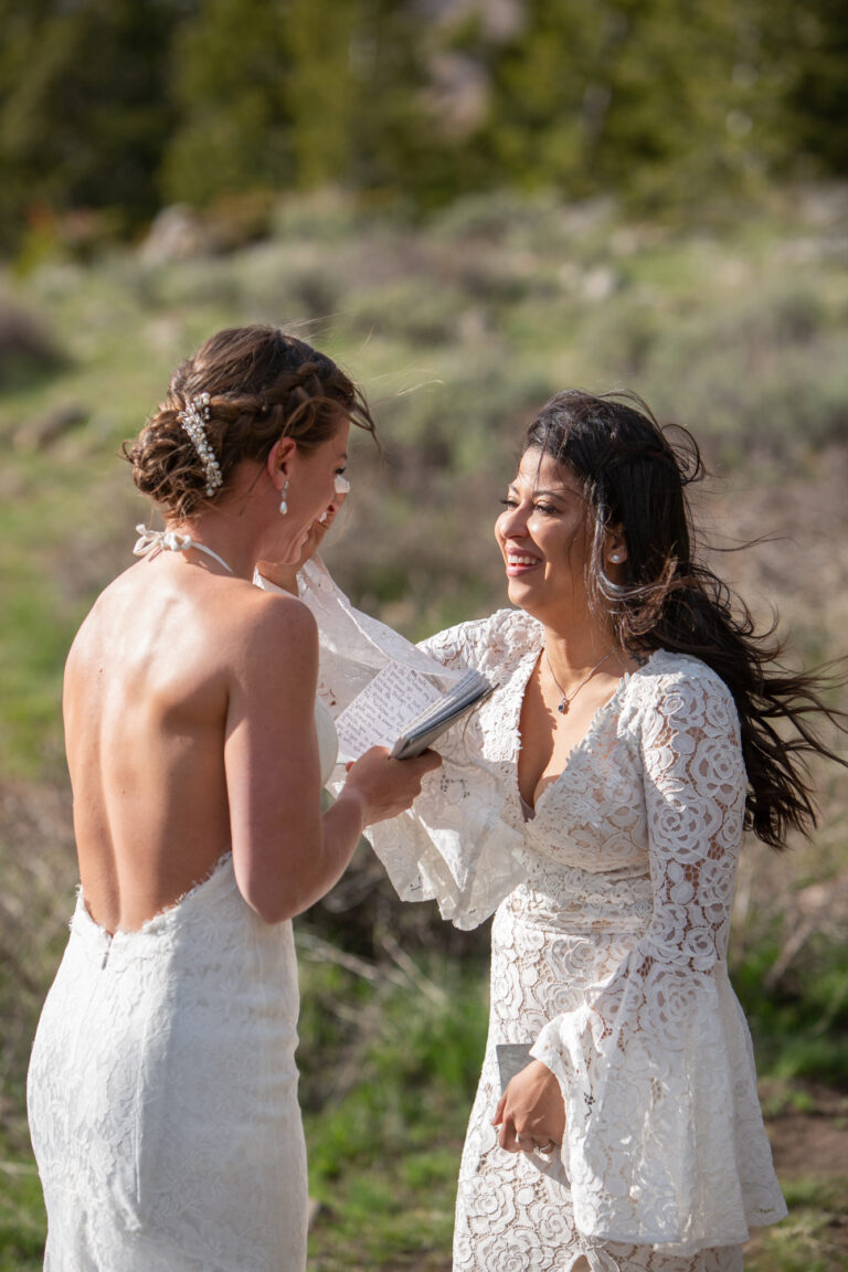 A bride wipes away her partner's tears as she reads her wedding vows to her bride on their Jackson Hole Elopement day.
