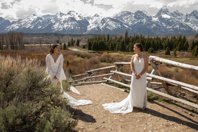 Brides turn towards each other during their first look, with snow capped Grand Teton mountains in the background.