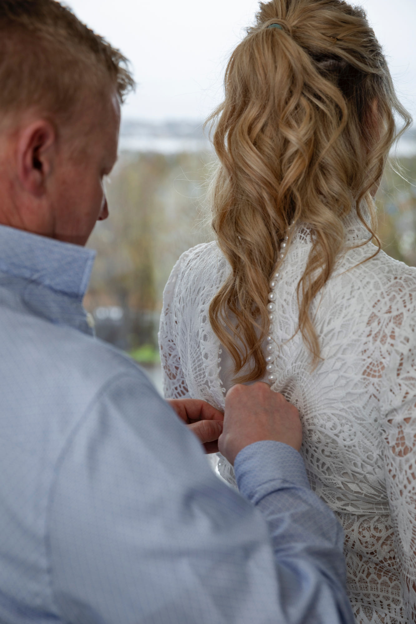 A groom buttons up the pearl buttons on the back of his bride's wedding dress.