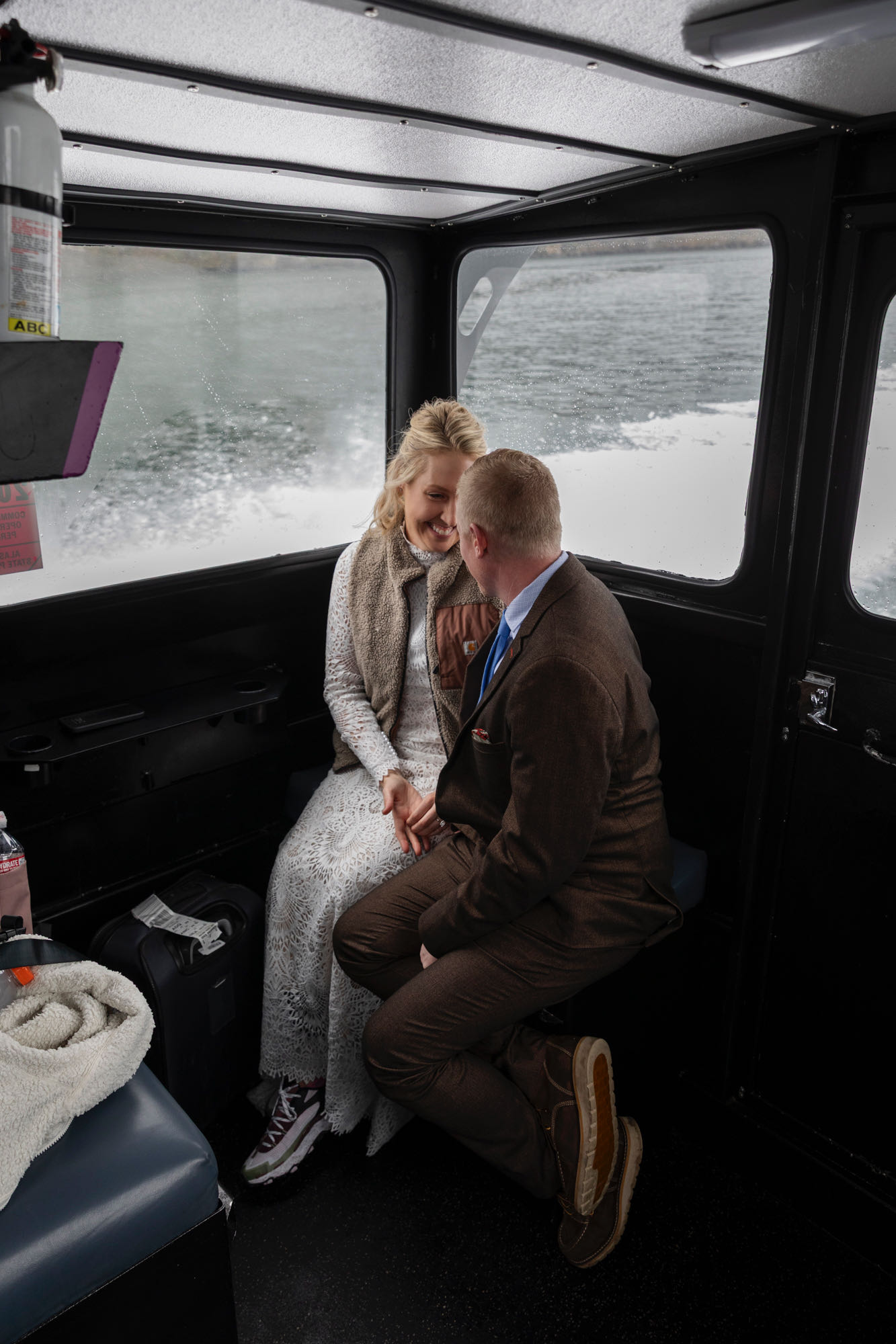 A bride and groom sit side by side on a boat, smiling at each other on their elopement day. 