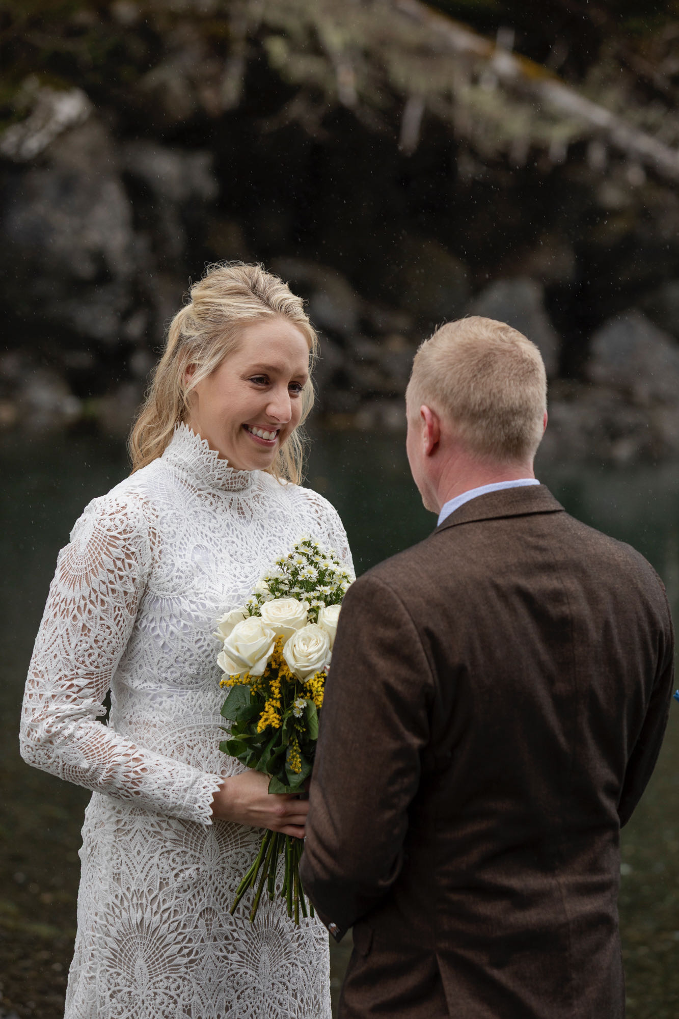 Bride holding bouquet and smiling during intimate Alaska elopement ceremony by the water