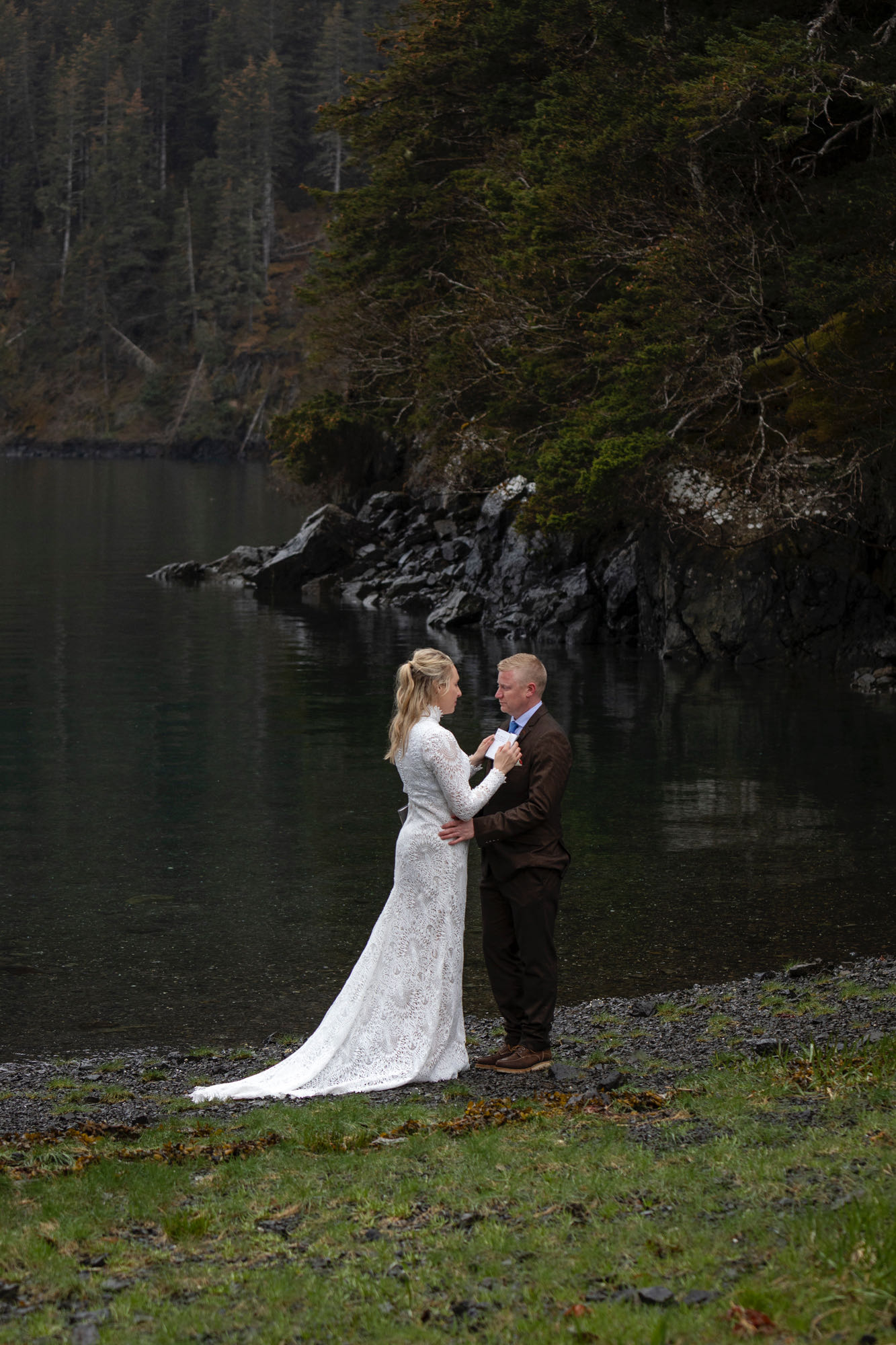 Couple standing together along forested shoreline during Kachemak Bay elopement in Homer Alaska