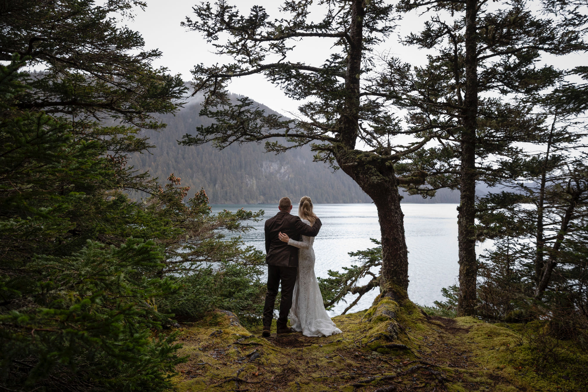 Couple sharing a quiet moment on forested bluff above Kachemak Bay during intimate Alaska elopement