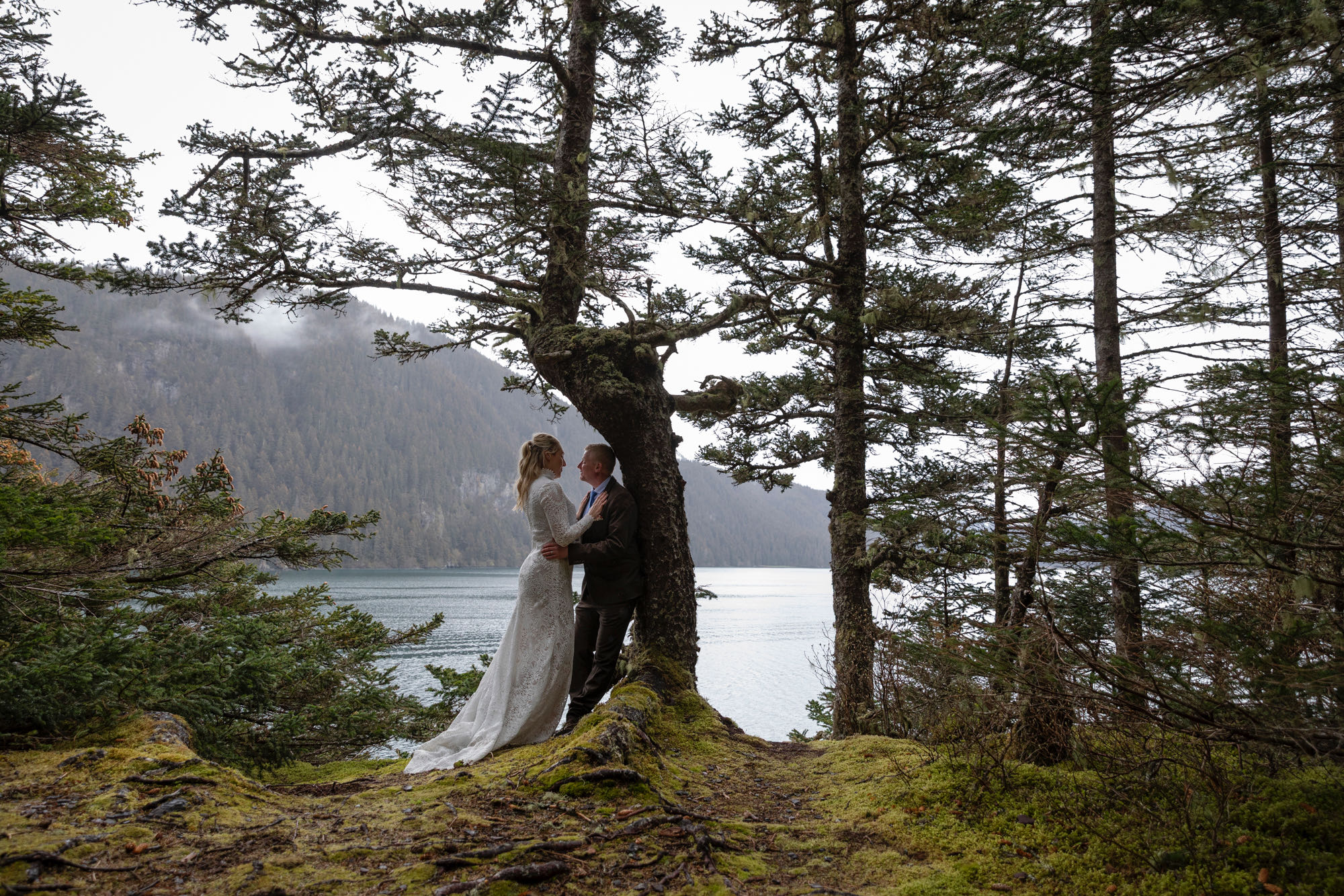 Couple embracing beneath trees along coastal forest during Kachemak Bay elopement in Homer Alaska