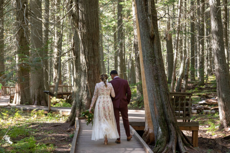 A bride and groom walk down a wooden boardwalk together during their leave no trace elopement in Glacier National Park