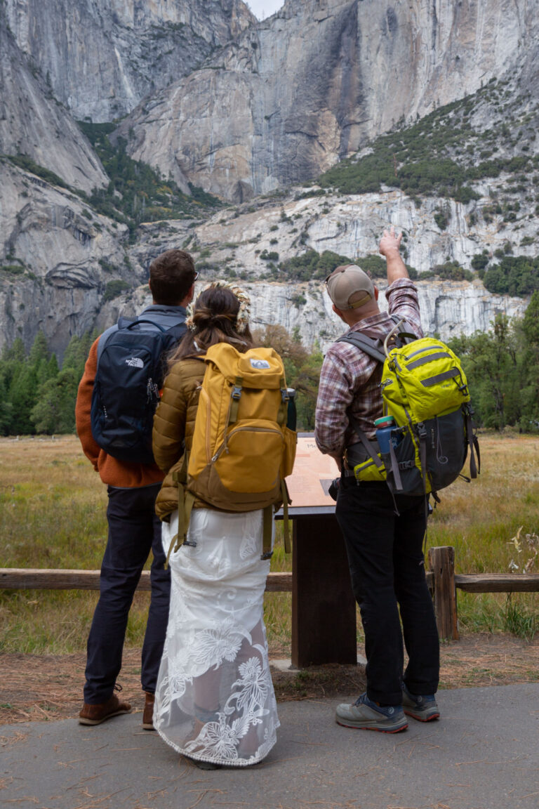Brian stands next to a bride and groom in Yosemite valley wearing one of his must have camera accessories, his atlas backpack