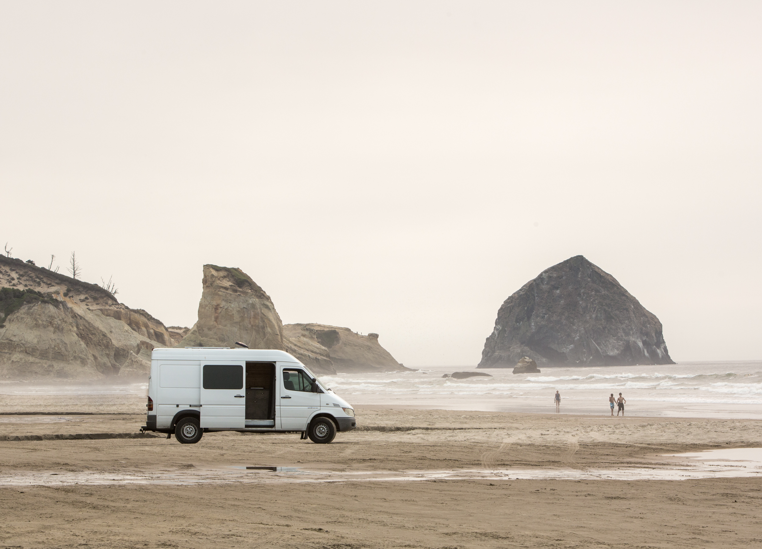 Oregon Coast Elopement Guide - How to Elope on the Oregon Coast | Scenic Vows A white van is parked on the Oregon Coast beach with the side door open and giant boulders raising in the background.
