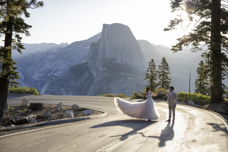 10 Breathtaking Places in California to Elope | Scenic Vows A bride and groom dance in the middle of the road in Yosemite National Park, with Half Dome in the background.