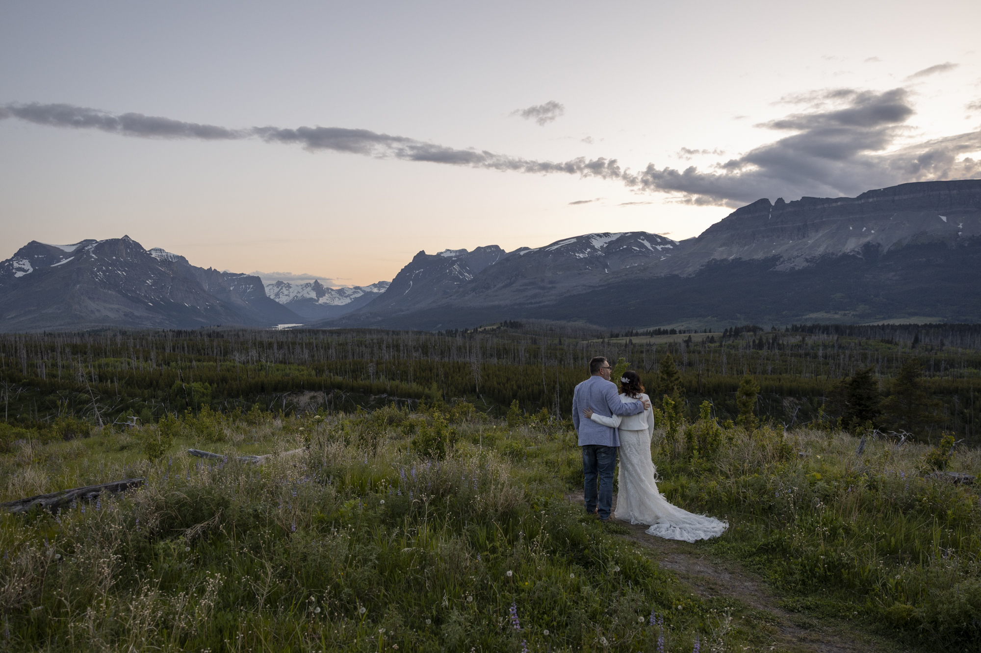 Forest Elopement Guide: Locations, Permits, and Tips for Your Adventure Ceremony | Scenic Vows A bride and groom stand with their arms around each other watching the sunset behind the mountains on their forest elopement day.