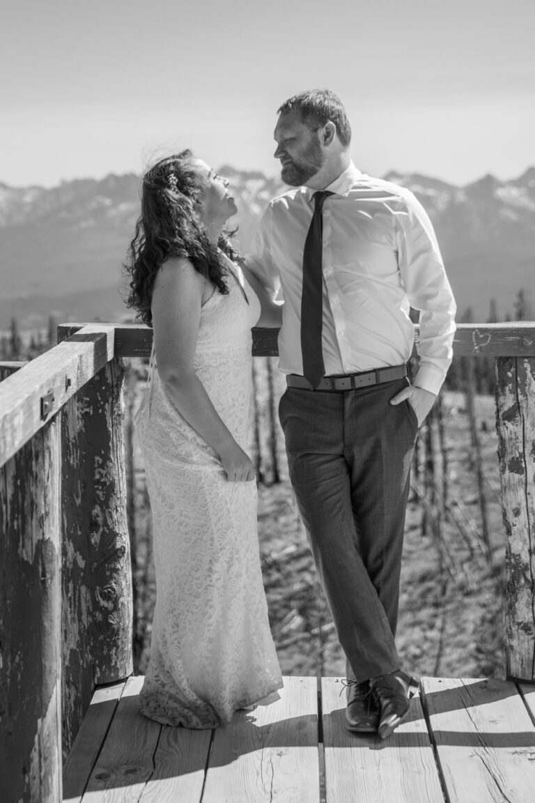 A bride looks up at her groom smiling as they stand on a wooden deck on their Stanley Idaho elopement day.