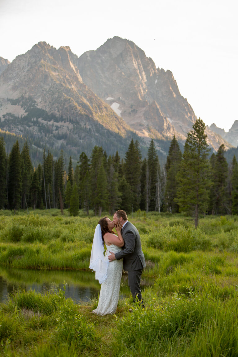 A bride and groom share their first kiss while standing in a grassy field