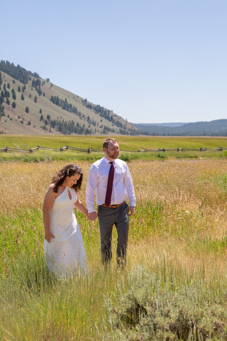 A bride and groom stand holding hands in a grassy field on their Stanley Idaho Elopement day.