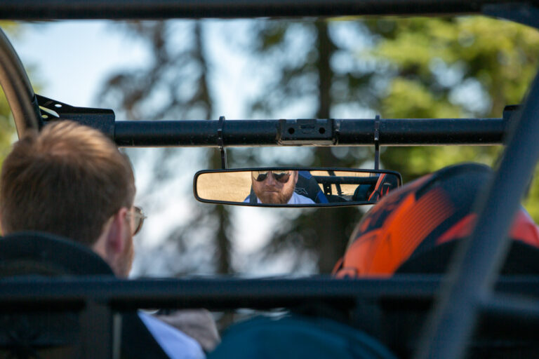 A man driving a side-by-side looks into the rear view mirror.