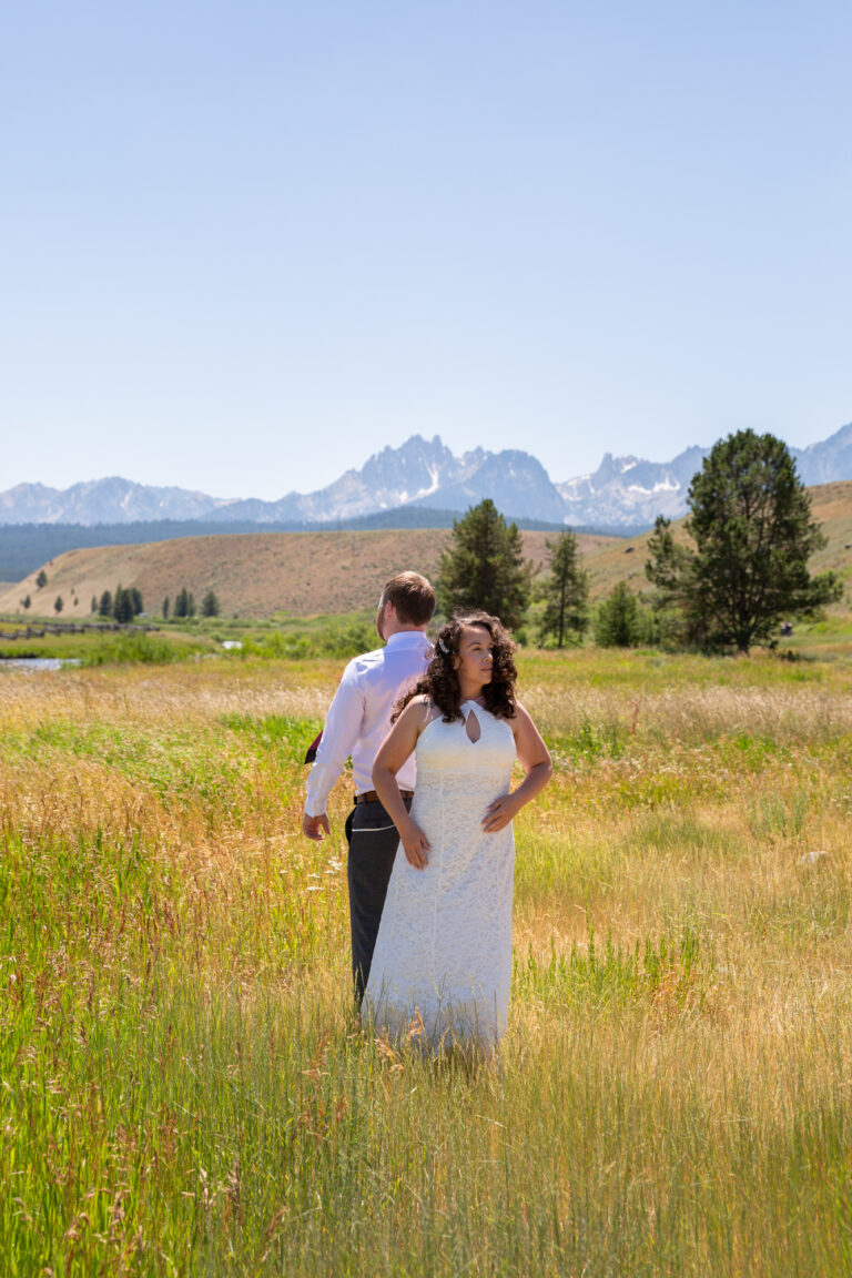A bride and groom stand back to back about to perform their first look during their Stanley Idaho elopement.