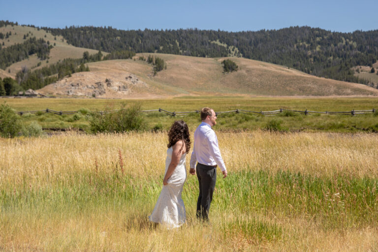 A bride and groom stand back to back in a grassy meadow on their Stanley Idaho elopement day.