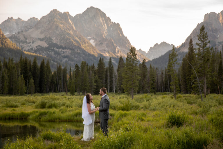 A bride and groom stand facing each other holding hands after their Stanley Idaho elopement ceremony.