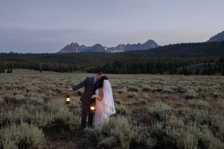 A bride and groom kiss while holding lanterns as the sunsets on their Stanley elopement day.
