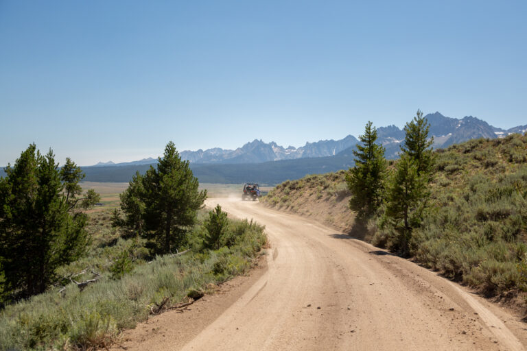 A side-by-side turns a corner on a dirt road in Stanley Idaho with the Sawtooth Mountain range in the background.
