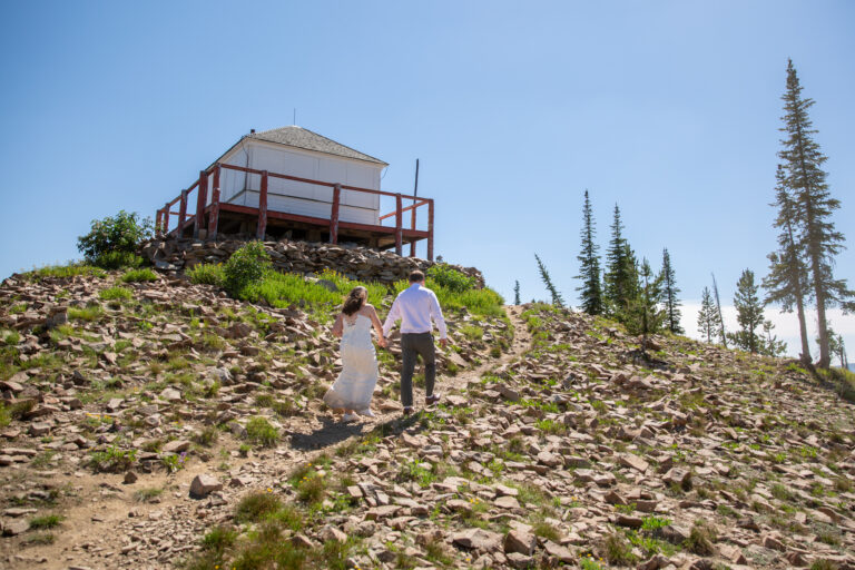 A bride and groom walk up a dirt path toward a Fire lookout on their Stanley Idaho elopement adventure.