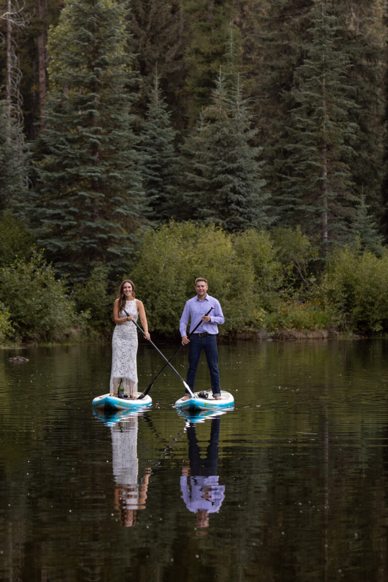 A bride and groom paddle on paddle boards across a lake on their wedding day.