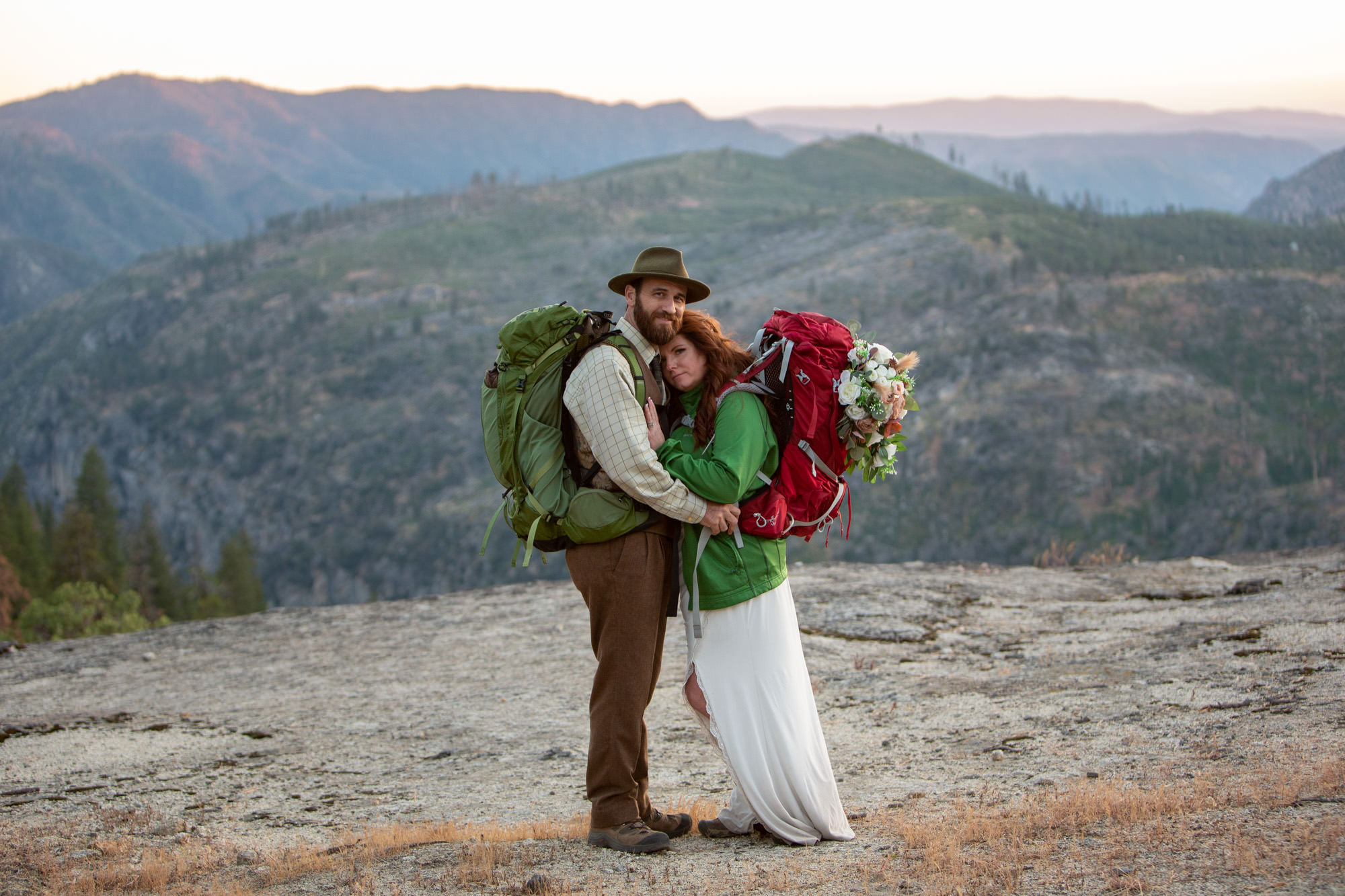 A bride and groom stand together with backpacks as the sunsets after their ceremony where the Yosemite Wedding permits allowed them.