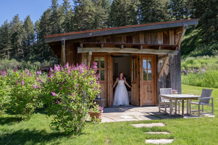 A bride opens the doors to a wood cabin and starts to walk outside.