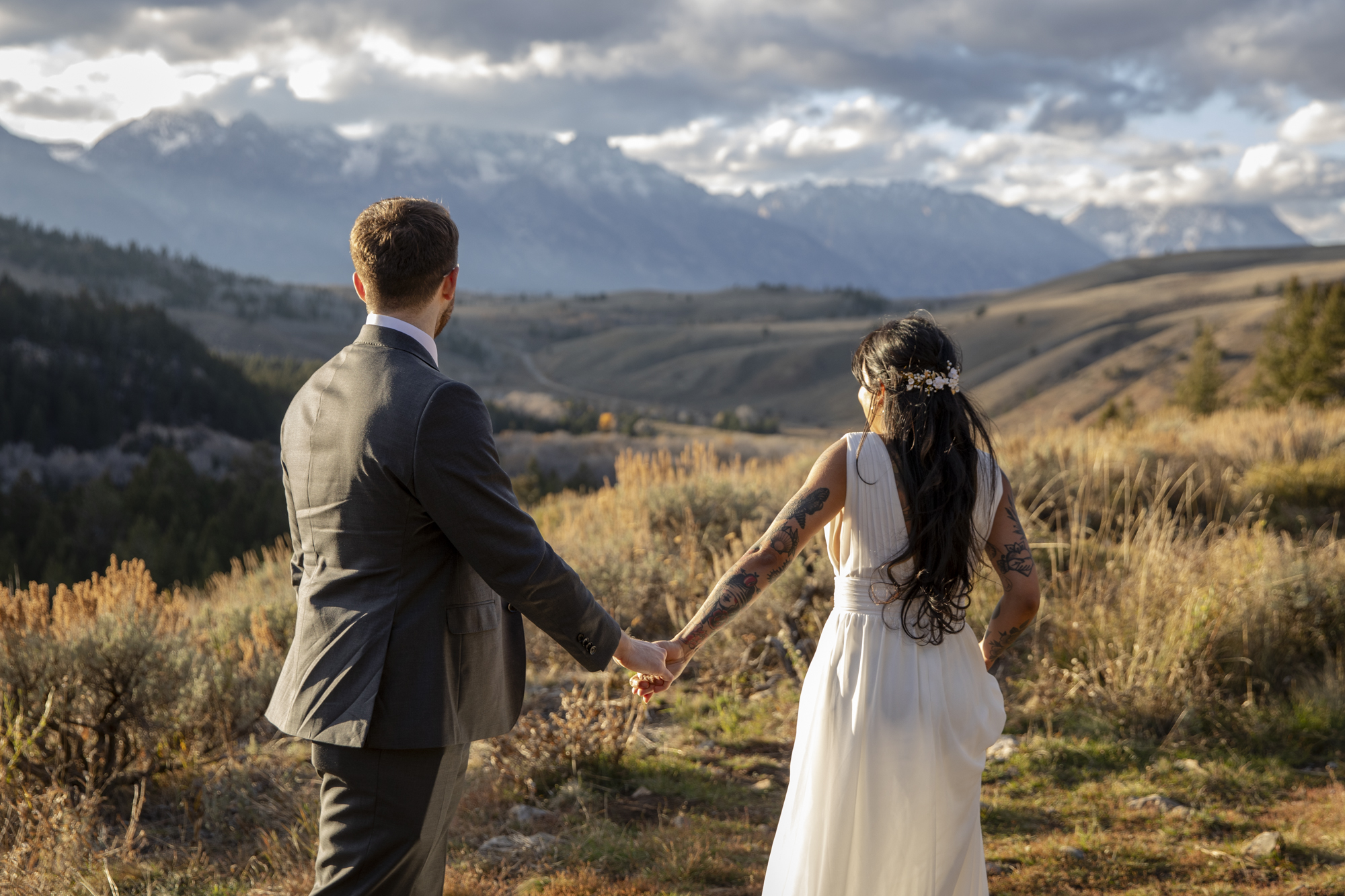 8 Incredible Places to Elope in Wyoming | Scenic Vows Newlyweds holding hands in Bridger-Teton National Forest with the Teton mountains in the distance