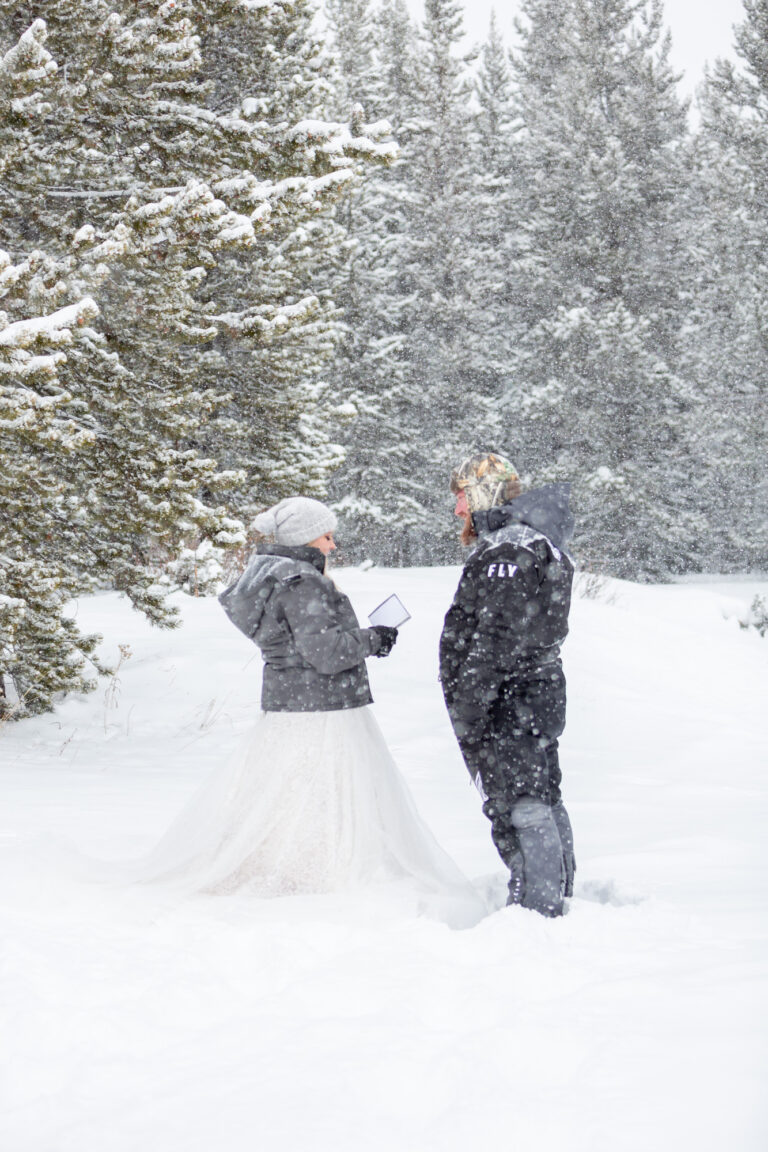 A bride reads her groom her vows from her vow book as the snow falls around them.