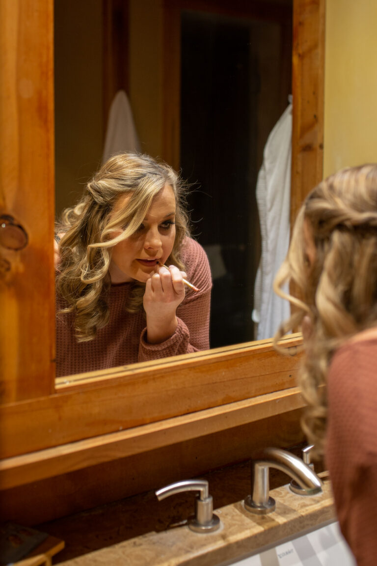 A woman applies lip liner while looking in a mirror.