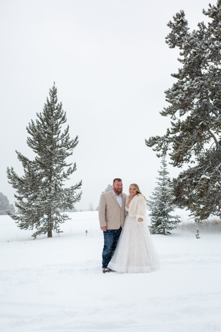 A bride and groom stand next to each other posing in the snow.