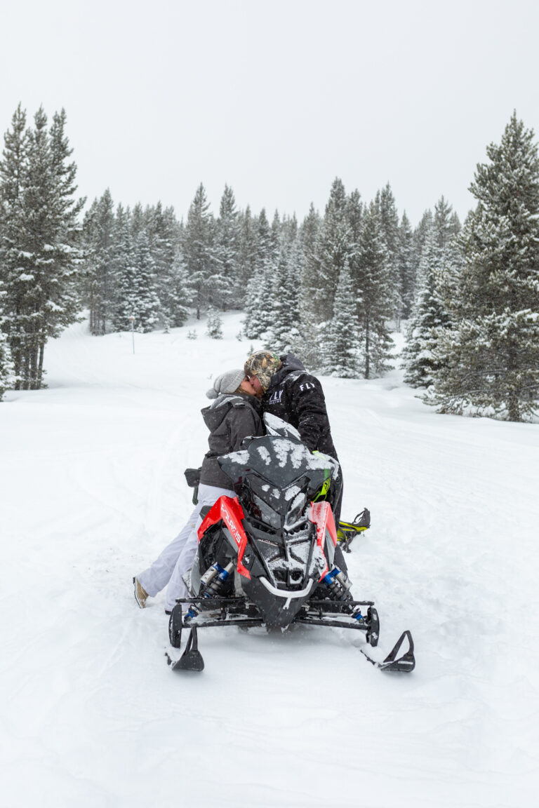 A bride and groom kiss over top of a snowmobile.