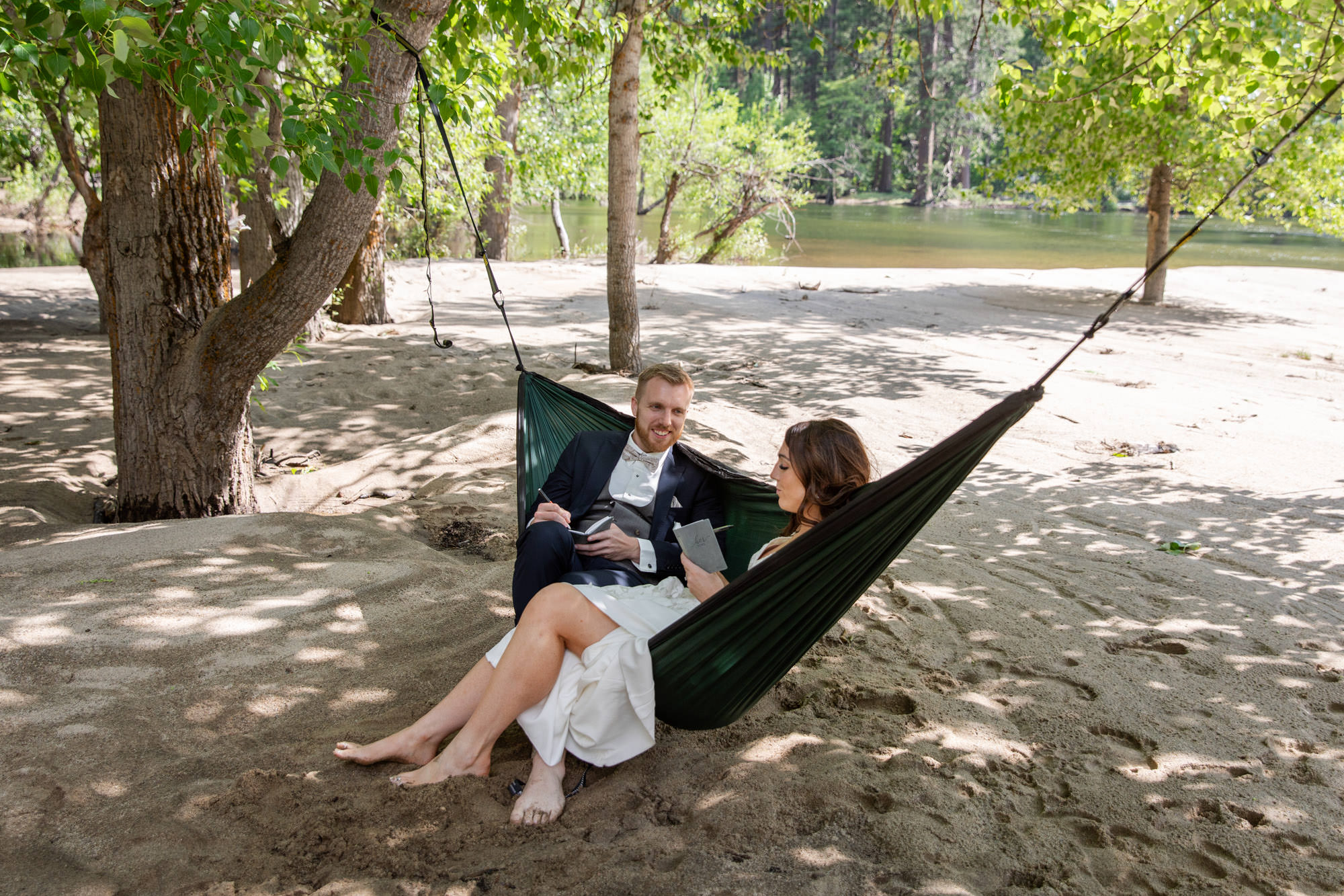 A bride and groom sit in a hammock together writing your wedding vows.