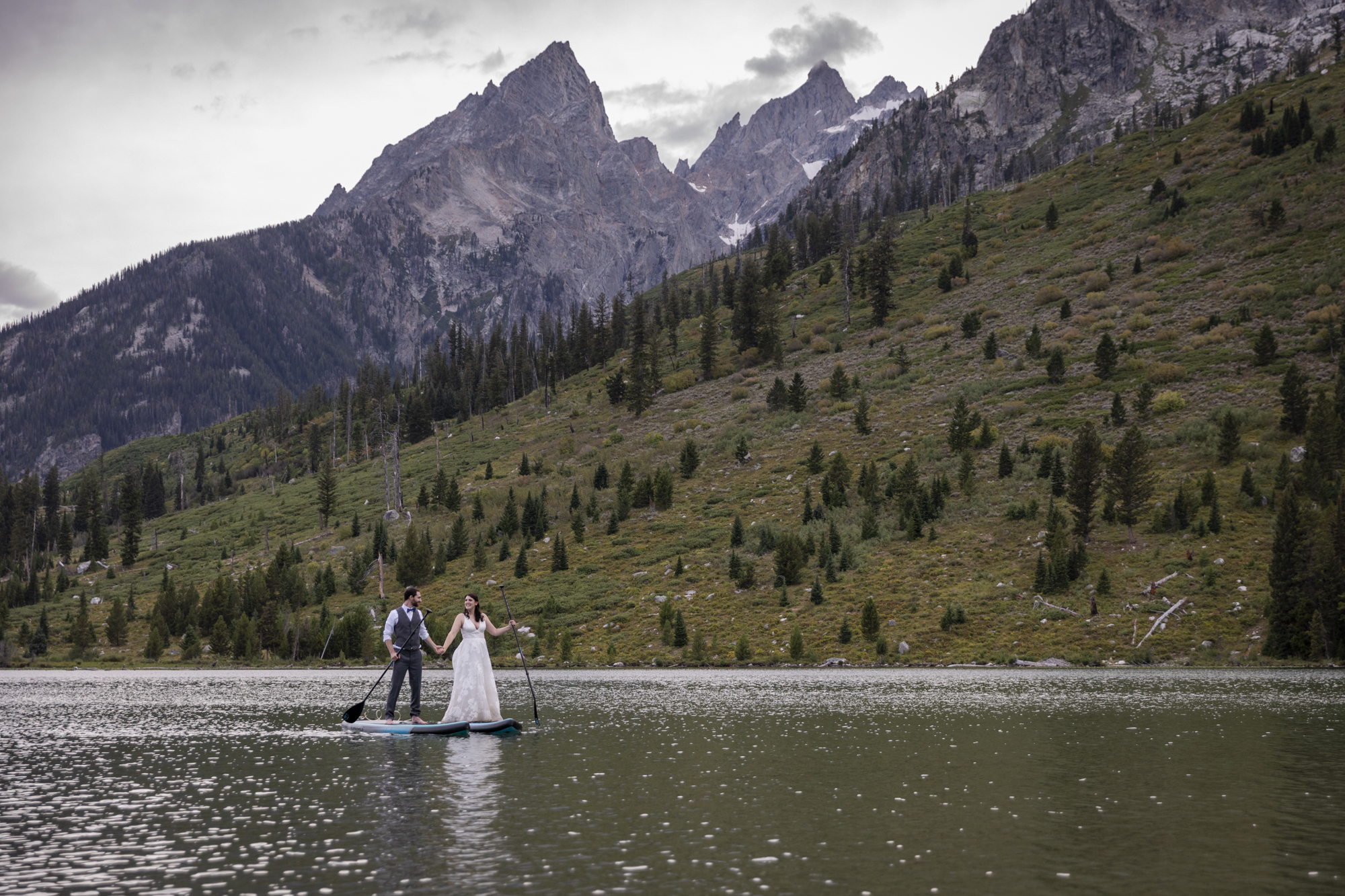 8 Incredible Places to Elope in Wyoming | Scenic Vows Bride and groom paddleboarding on an alpine lake at a scenic Wyoming elopement location