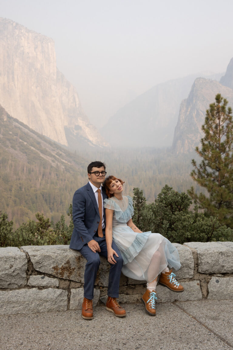 A bride and groom sit next to each other at Tunnel View in Yosemite on their elopement day.