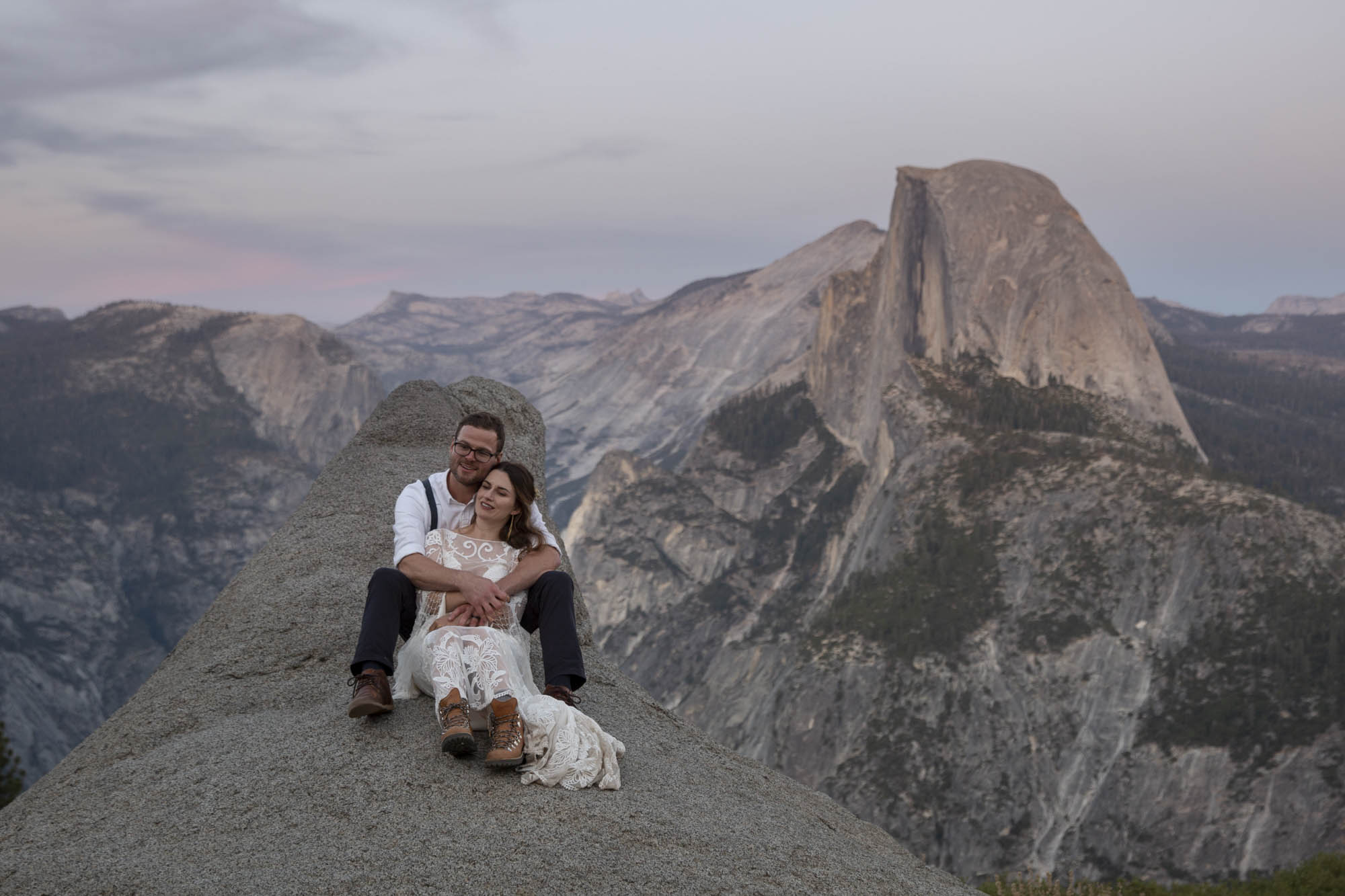 A groom sits behind a bride on a rock in Yosemite on their elopement day at Glacier Point.